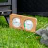 MOOSSE sauna thermometer naast een houtgestookte kachel, een vuurpoker en een berg saunastenen.