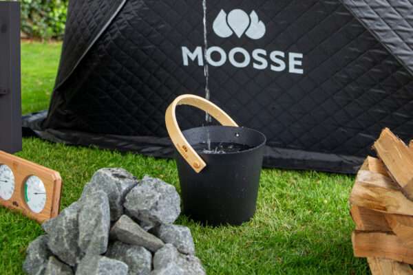 Aluminum MOOSSE sauna emmer waar water in wordt gegiet, naast saunastenen, kachelhout en een thermometer